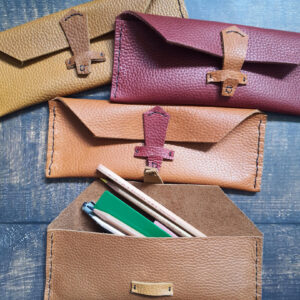 Four leather pencil cases in orange/yellow/red colours, with leather latches. One is open to show the stationery inside.