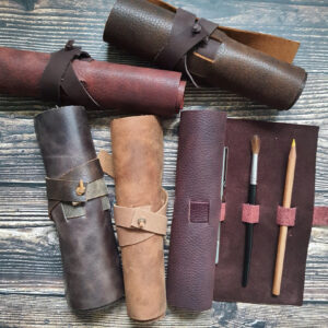 Five leather pencil rolls in various earthy colours. One is half unrolled, showing the stationery inside.